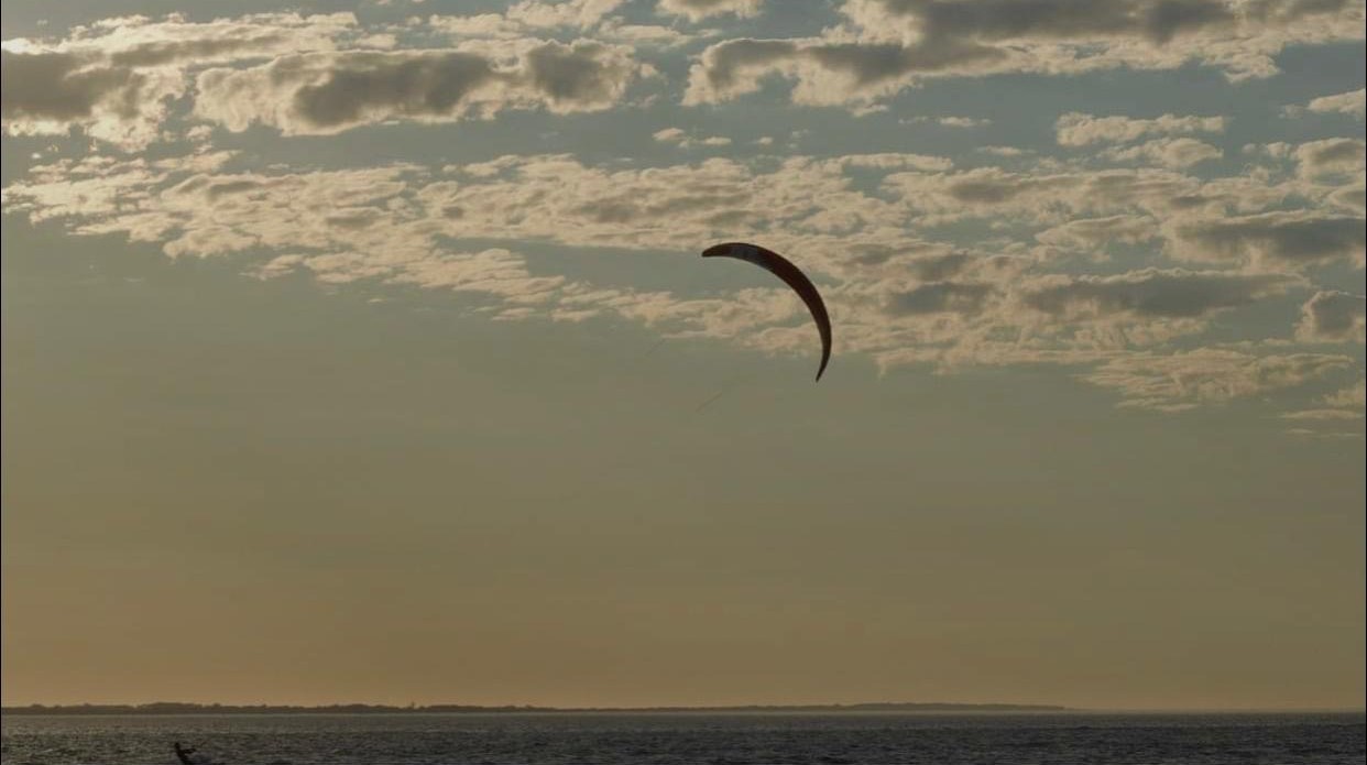 A paraglider suspended against a golden coastal sky at dusk, photographed by KTG SNVPS