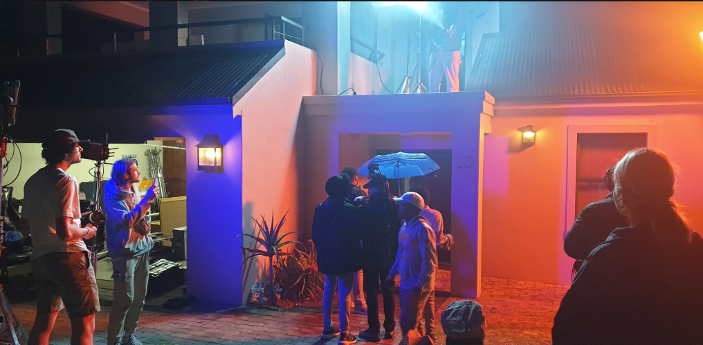 Night commercial set lit in blue and amber, crew working around the doorway