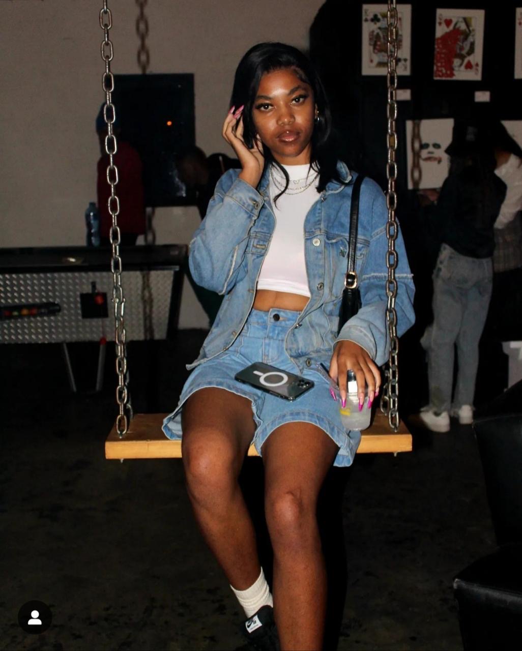 Guest seated on a wooden swing in denim, holding a drink