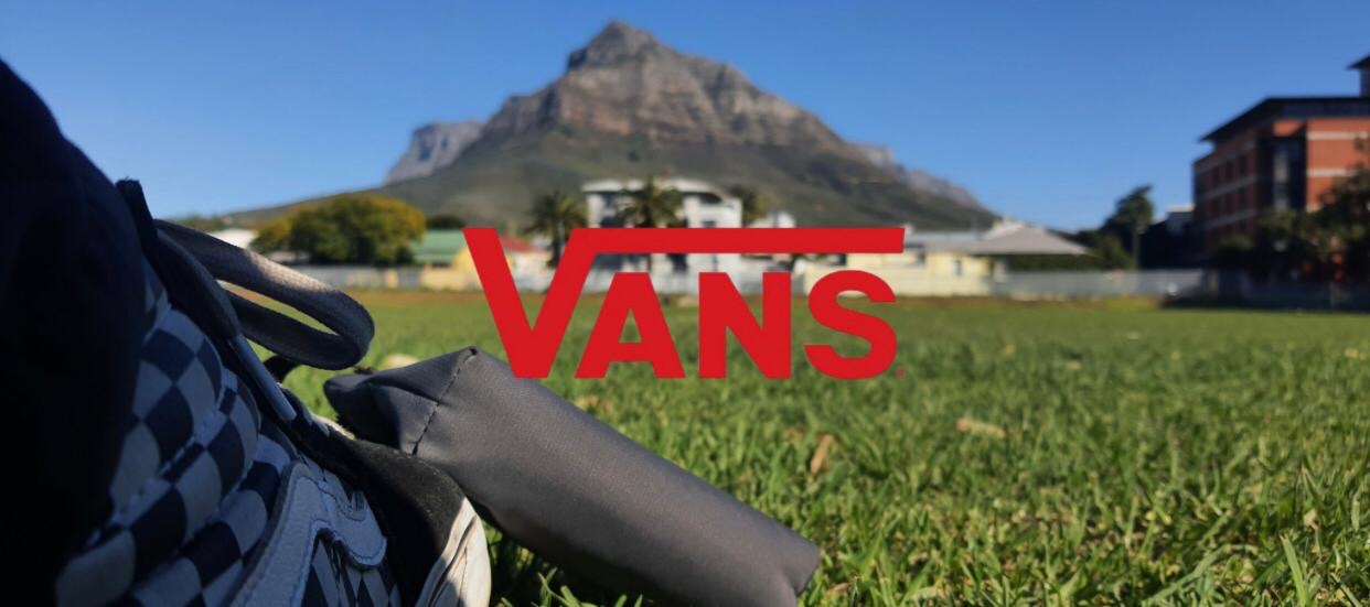 Vans checkerboard shoe on grass with Table Mountain behind, red Vans logo across the frame
